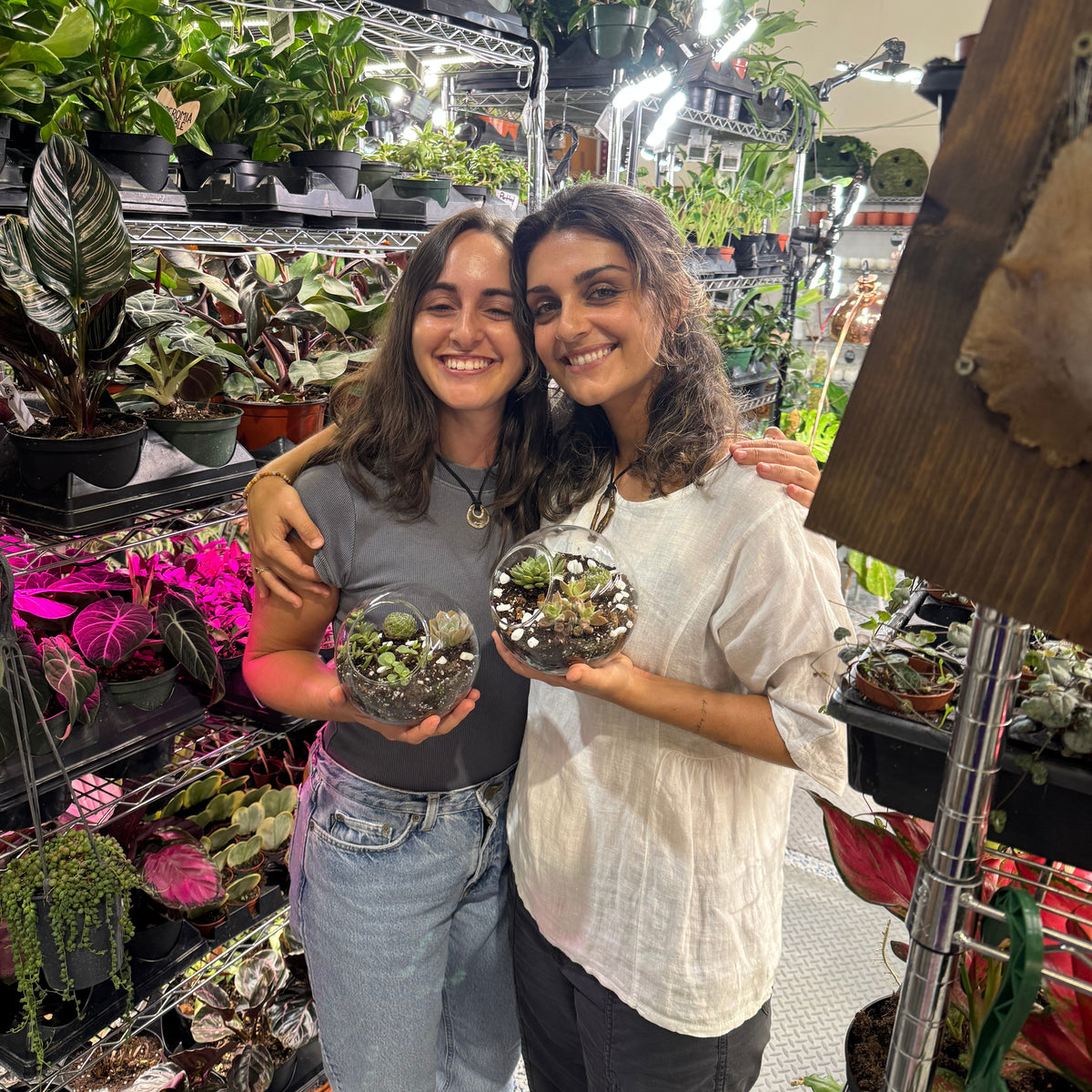 Two women holding small plants in a garden center.