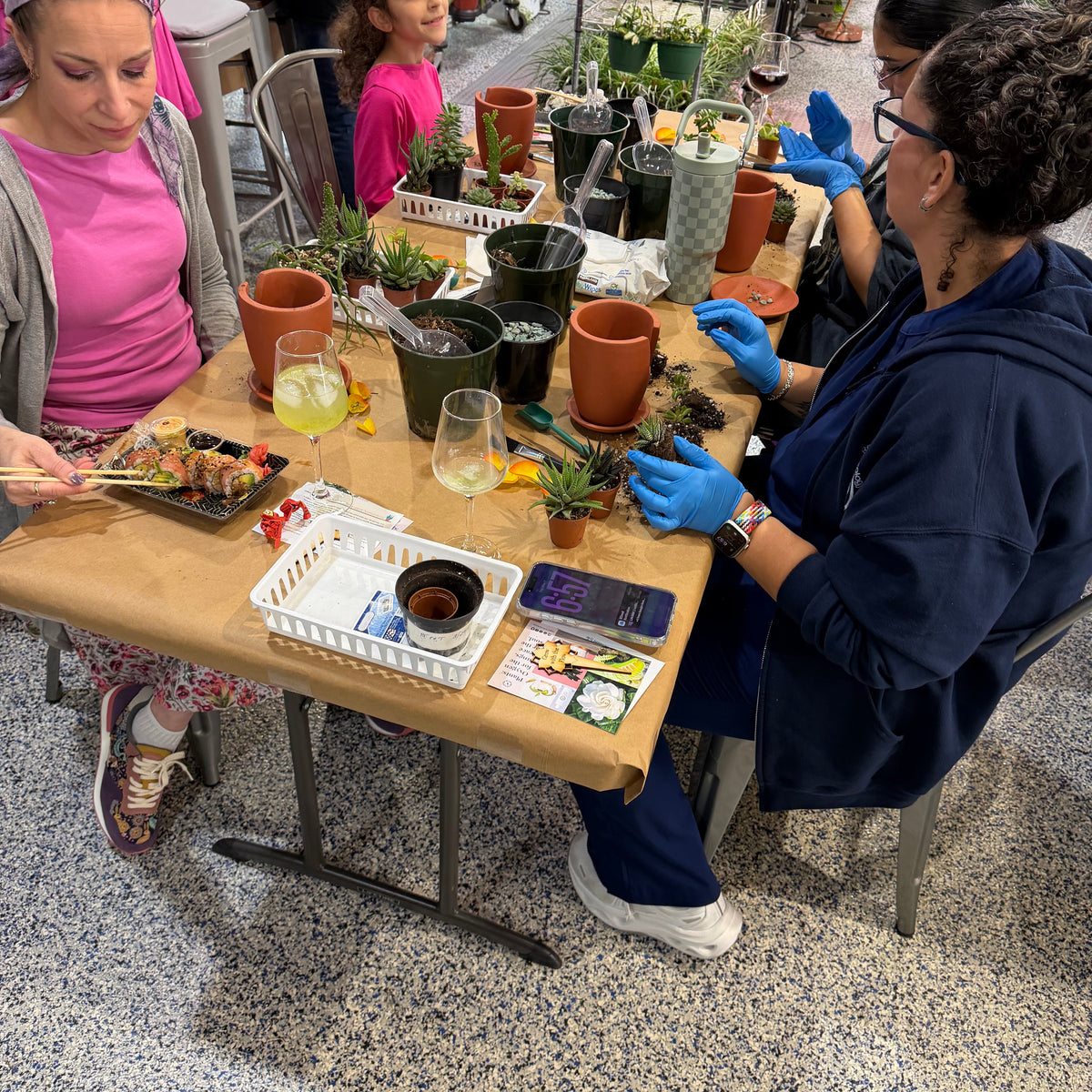 People at a table with potted plants and gardening supplies in an indoor setting