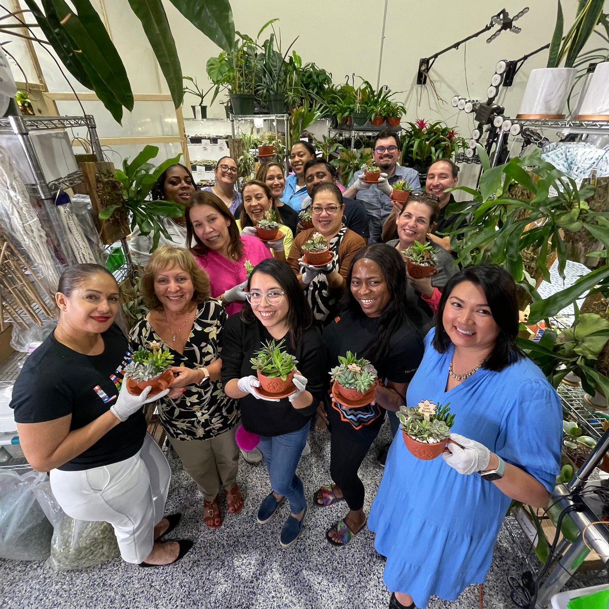Group of people holding small plants in a greenhouse setting