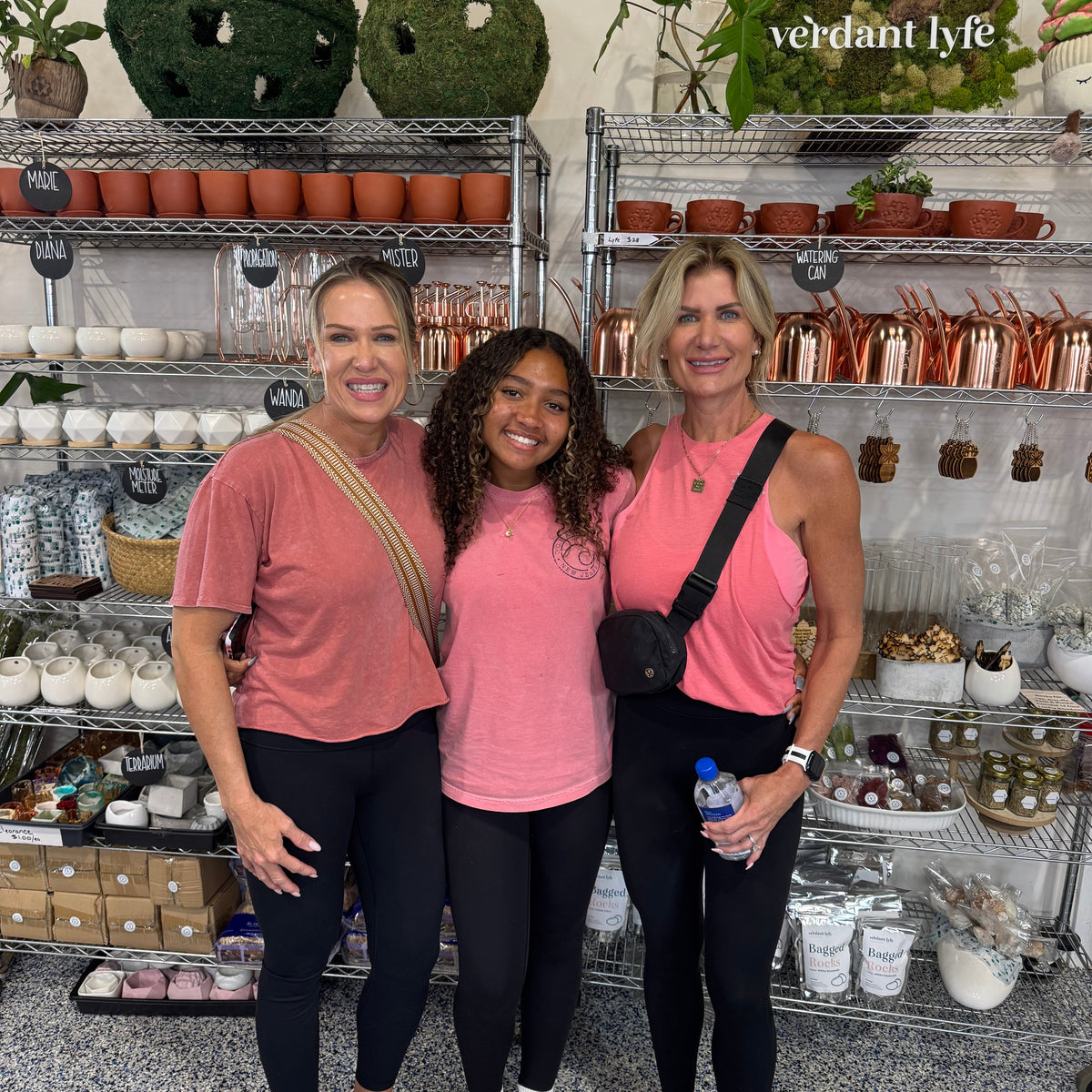 Three women posing together in a store with shelves of products and plants.